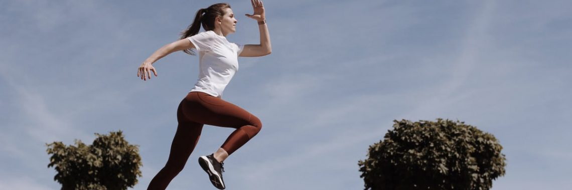Athletic woman running on an outdoor road, demonstrating fitness and determination under a blue sky.
